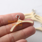 Handmade miniature wooden clothes hanger with silver metal hook held between two fingers, showing wood grain detail and true scale, additional hangers blurred in background