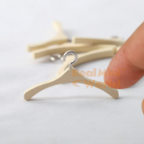 Handmade miniature wooden clothes hanger with silver metal hook held between two fingers, showing wood grain detail and true scale, additional hangers blurred in background