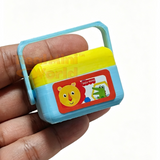 Miniature working shape sorter with yellow lid and blue body resting on an open palm, with 10 tiny colorful shape pieces — stars, cubes, cylinders, triangles — scattered in the hand below it